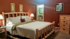 Un lit en bois avec du linge de lit blanc, une table de chevet, une commode et des tableaux encadrés au mur.