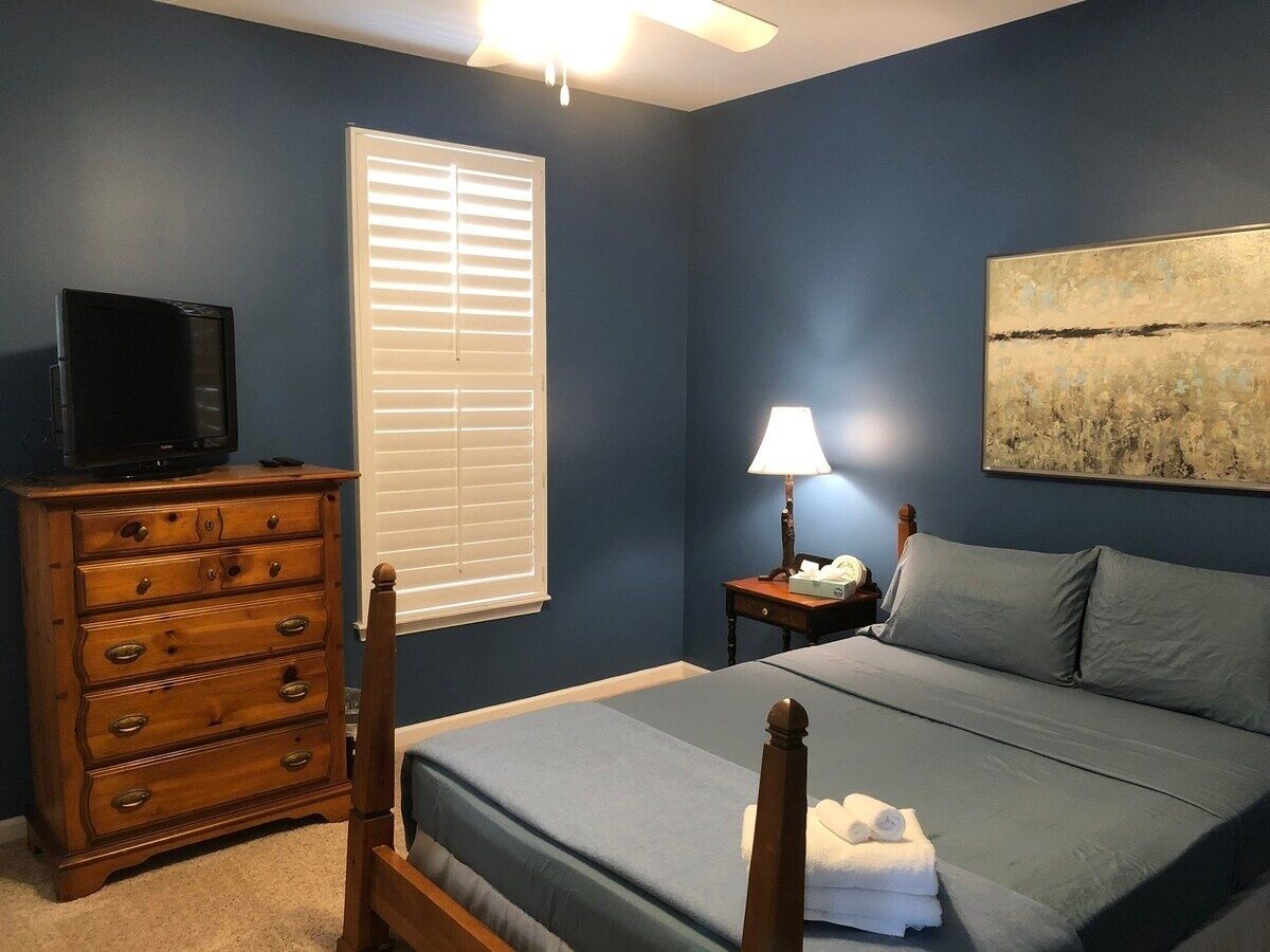Quarto com cama, cômoda, mesa de cabeceira, luminária e um quadro na parede.