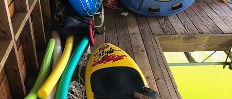 A wooden deck with a kayak, a blue inflatable raft, and a blue inflatable boat.