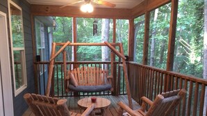Une terrasse en bois avec une balançoire, un banc et deux fauteuils à bascule.