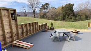 A covered patio area with a wooden deck, a picnic table, benches, and a fire pit.