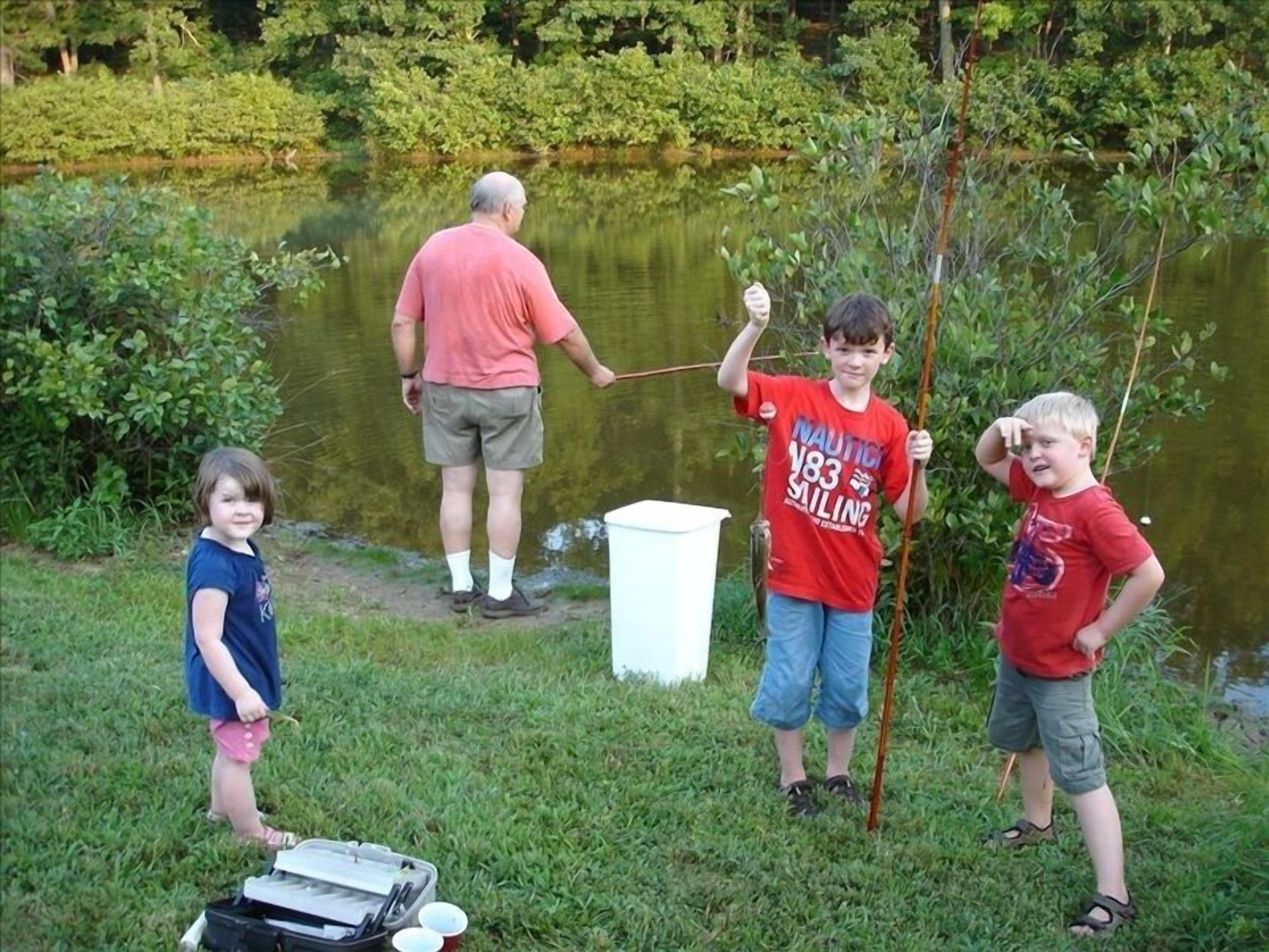 A group of people by a pond, one holding a fish.