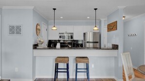 A modern kitchen with white cabinets, stainless steel appliances, and two bar stools with woven seats. - Award-Winning Resort Amenities | Lagoon Villa 21 (Isle of Palms)