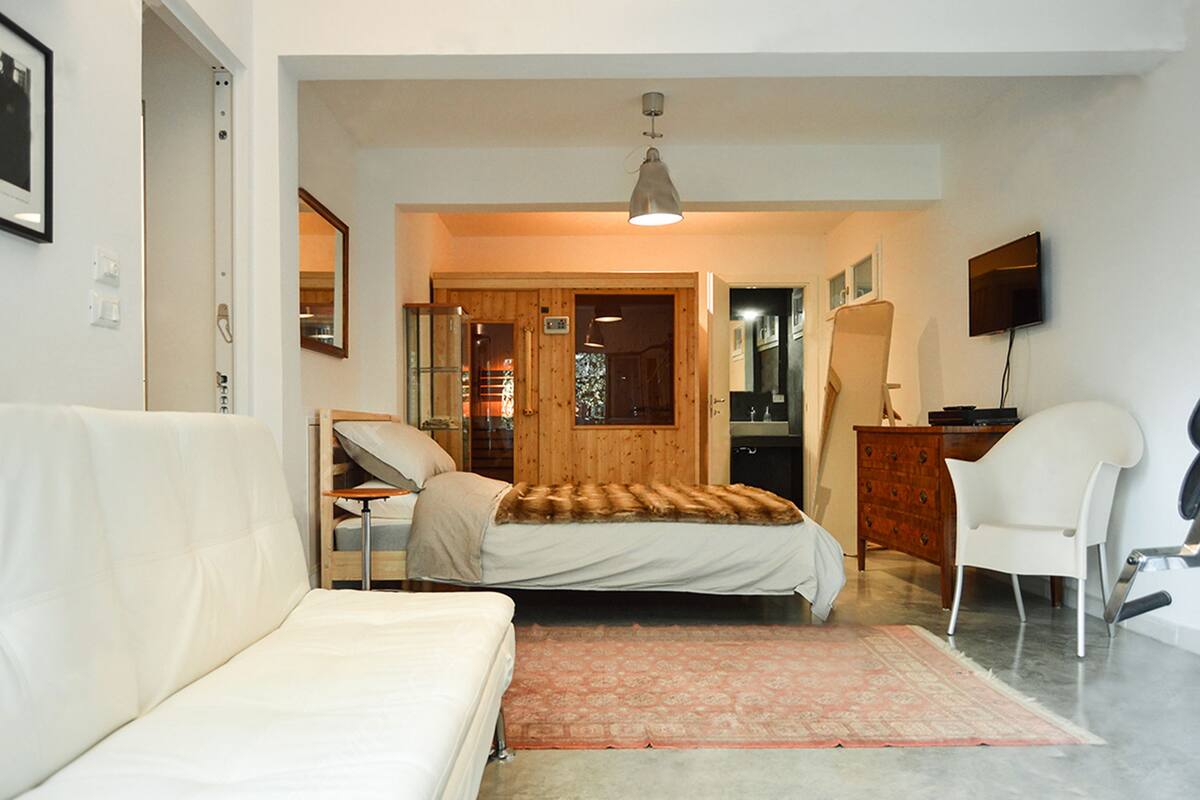 A bedroom with a bed, a sofa, a wooden wardrobe, a television, and a mirror.