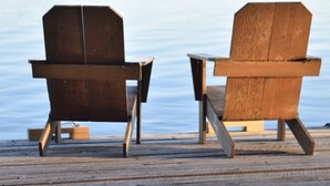 Dos sillas Adirondack de madera sobre un muelle de madera junto a un lago tranquilo.