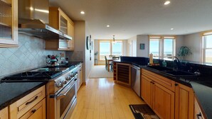 A modern kitchen with wooden cabinets, a stainless steel range, and a large island with a sink. - OCEAN FRONT: SEAVIEW SERENITY: Seaside Vacation Homes, Inc Managed  (Seaside)
