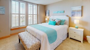 A bedroom with a large bed, a bench, a nightstand with a lamp, and artwork on the walls. - OCEAN FRONT: SEAVIEW SERENITY: Seaside Vacation Homes, Inc Managed  (Seaside)