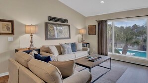 A living room with a sofa, coffee table, and two lamps. There is a large window with a view of a swimming pool.
