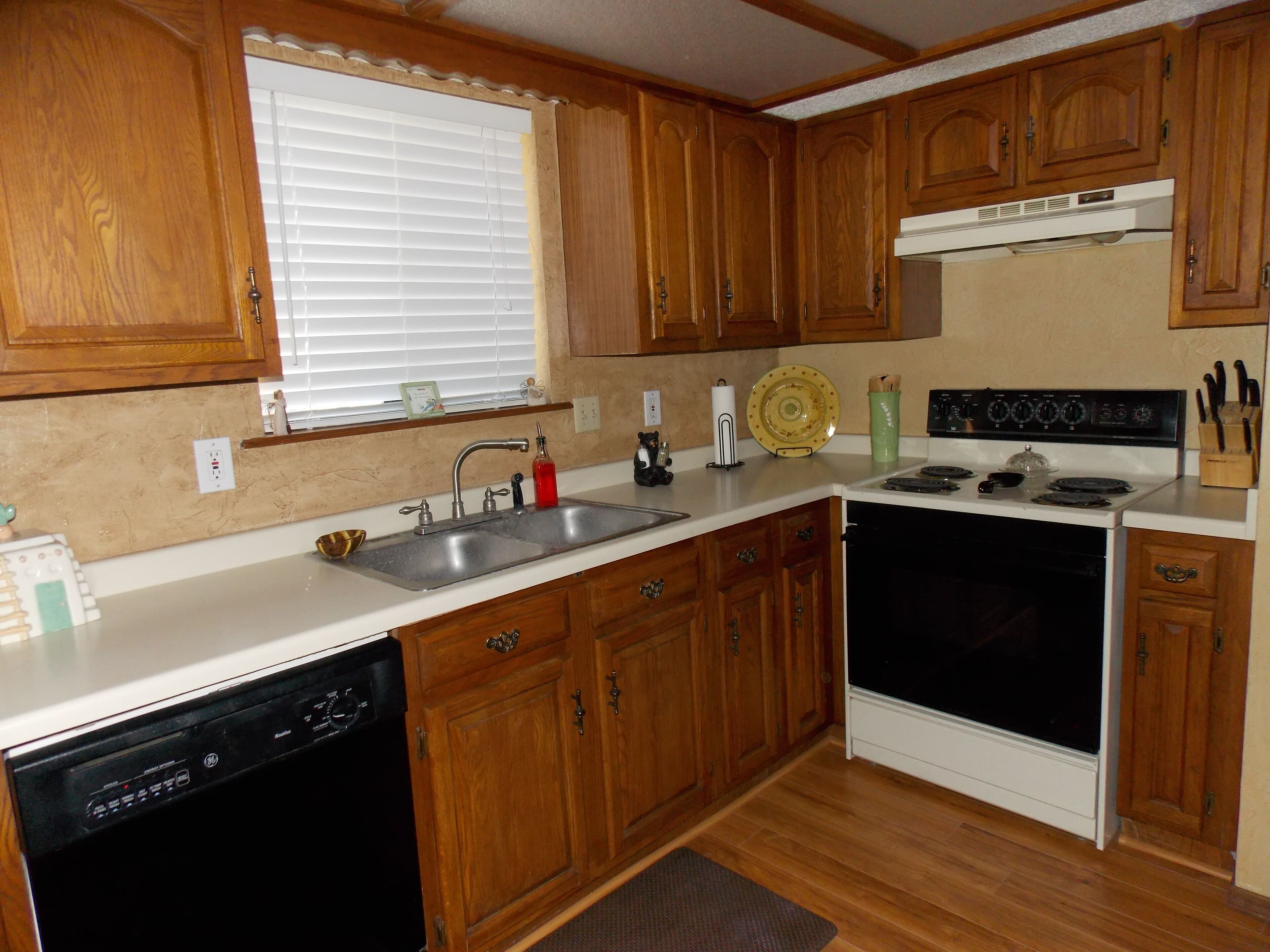A kitchen with wooden cabinets, a dishwasher, a stove, and a window with blinds.