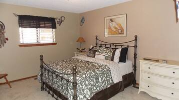 A bedroom with a four-poster bed, a bedside table with a lamp, a dresser, and a wall-mounted painting.
