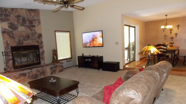 A living room with a stone fireplace, a television, a sofa, a dining area with a table and chairs, and a ceiling fan. - New furniture Beautiful Home! (Ruidoso)