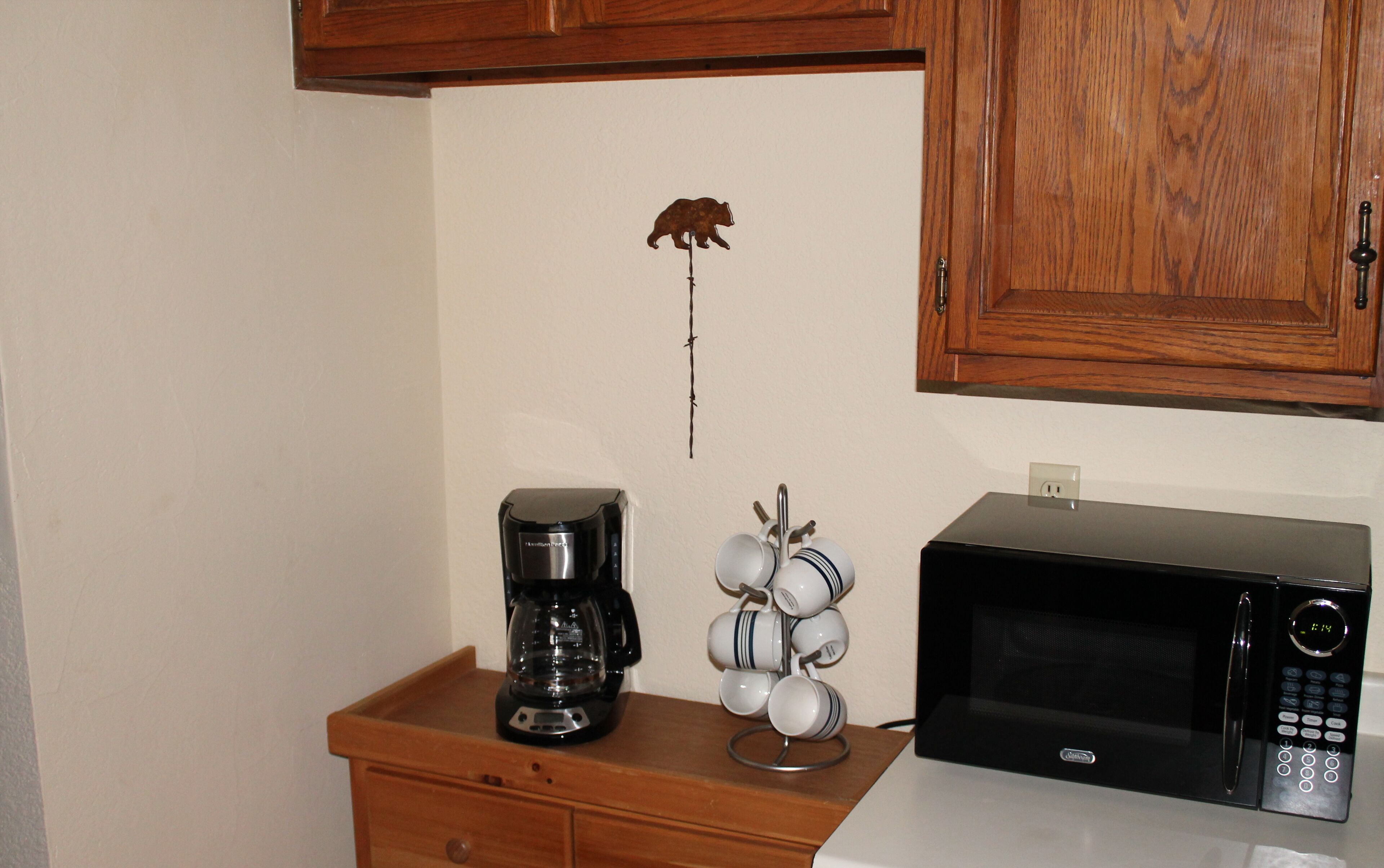 A kitchen with a coffee maker, a mug rack, and a microwave.