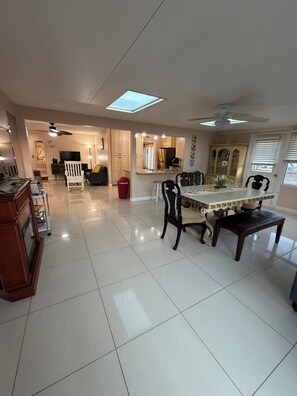 A spacious living area with a dining table, chairs, a TV, and a ceiling fan.