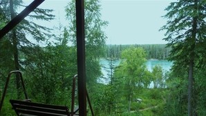 A wooden bench overlooking a lake surrounded by dense forest. - Kenai Riverfront Cozy Studio (Soldotna)