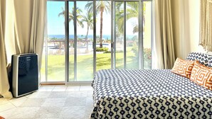 A bedroom with a large bed, a ceiling fan, and a view of a pool and palm trees through a sliding glass door.