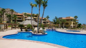 A resort pool area with palm trees, a thatched-roof structure, and a clear blue pool.