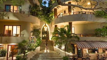 Hotel com vários níveis, uma escadaria central, área de estar externa e vegetação exuberante.