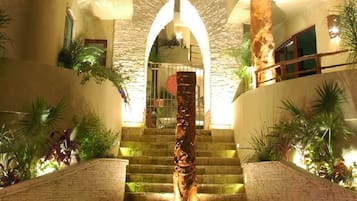 Una escalera con una columna central, rodeada de plantas y paredes de piedra.