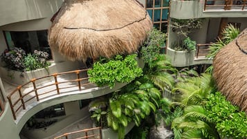 Um resort com várias estruturas de telhado de palha, uma piscina central e vegetação exuberante.