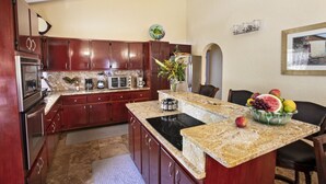 A kitchen with dark wooden cabinets, a granite countertop, a built-in stove, and a fruit bowl on the island. - Ocean-View 3BR Villa for Families and Groups (St Thomas)