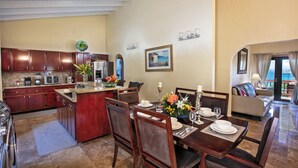 A spacious dining area with a large island, wooden chairs, and a view of the ocean through a balcony. - Ocean-View 3BR Villa for Families and Groups (St Thomas)