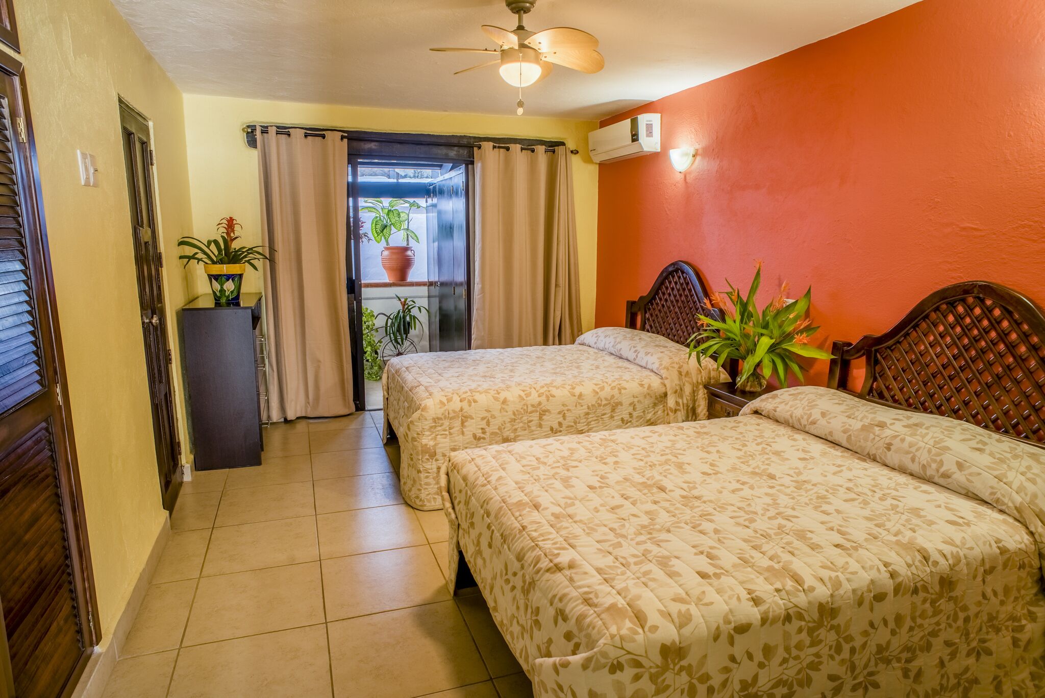 A hotel room with two beds, a ceiling fan, a potted plant, and a window with curtains.