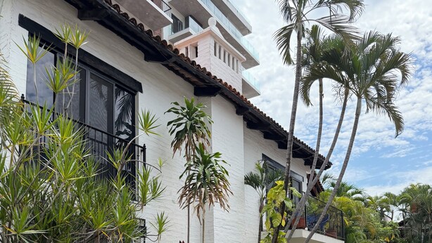 A modern building with balconies, surrounded by lush greenery and a well-maintained hedge.