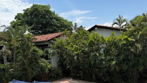 A swimming pool with lounge chairs and umbrellas, surrounded by lush greenery and a clear sky.