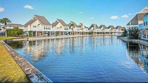 A residential area with houses along a water body, reflecting the buildings and sky. - Sandpiper Cove 1090 2bed 2bath Beach Service new FALL DATES available! (Destin)