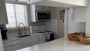 A modern kitchen with white cabinetry, a built-in microwave, an oven, and a sink. There is a sign on the wall that reads "JUST DAY IN." - Sandpiper Cove 1090 2bed 2bath Beach Service new FALL DATES available! (Destin)
