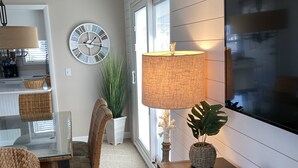 A dining area with a glass table, wicker chairs, a potted plant, a wall clock, and a TV mounted on the wall. - Sandpiper Cove 1090 2bed 2bath Beach Service new FALL DATES available! (Destin)