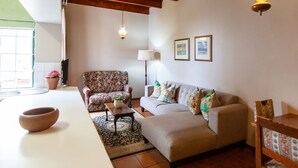 A living room with a sofa, armchair, and a table with a bowl. There is a ceiling fan, a lamp, and framed pictures on the wall. - The Habit Self Catering (Worcester)