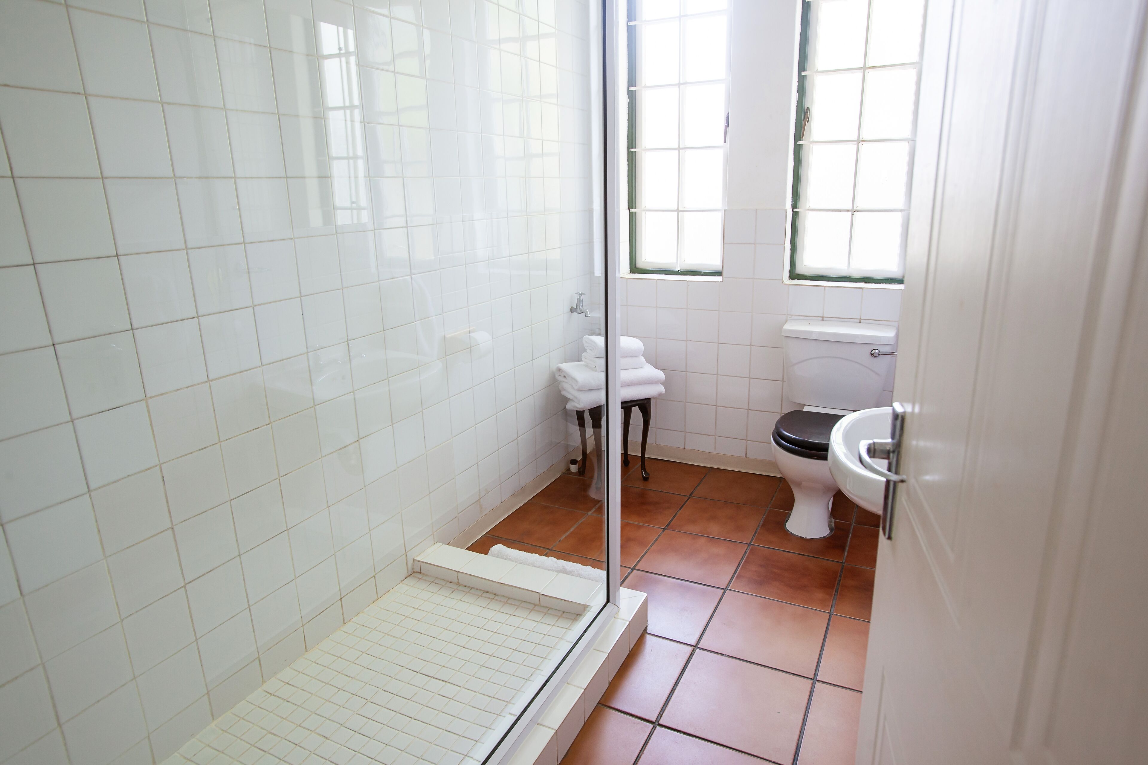 A bathroom with white tiled walls, a shower area, a toilet, and a window.