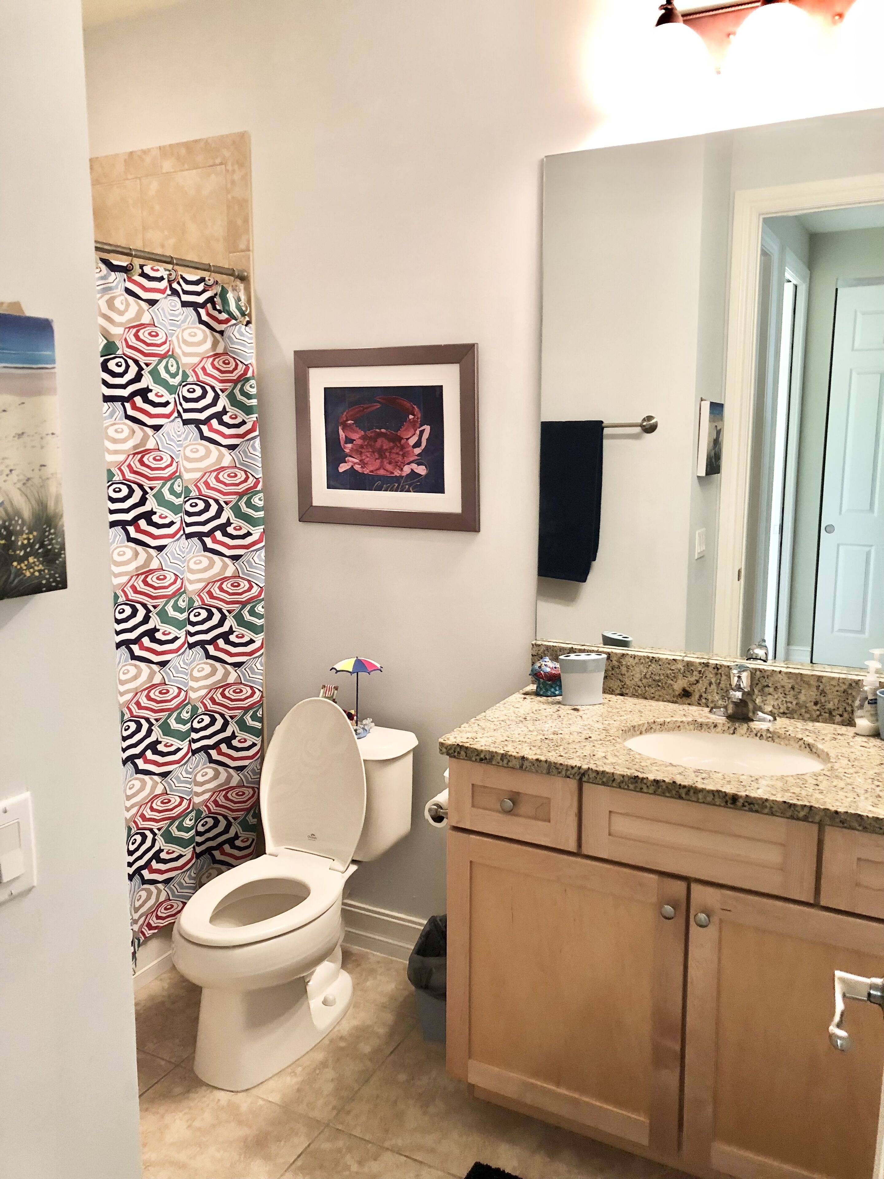Ein Badezimmer mit Toilette, Waschbecken und Spiegel. Ein gerahmtes Bild hängt an der Wand und ein Handtuch am Handtuchhalter.