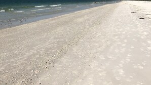 Una playa con una amplia orilla arenosa, mar tranquilo y nubes dispersas.