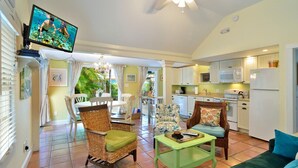 A compact living space with a dining area, kitchen, and a television displaying an underwater scene. - Key West Wabi Sabi - Authentic Downtown Cottage w Pool - Steps Off Duval (Key West)