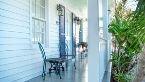 A covered porch with a table and chairs, a bird feeder, and potted plants. - Key West Wabi Sabi - Authentic Downtown Cottage w Pool - Steps Off Duval (Key West)
