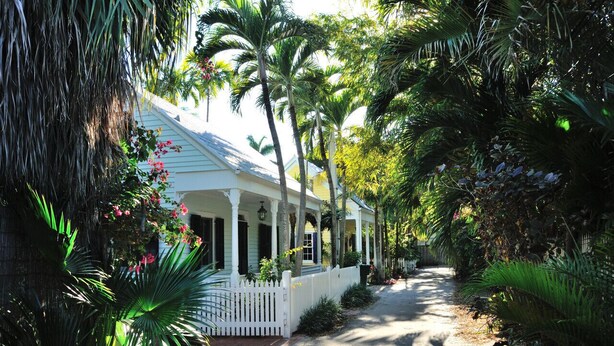A white house with a porch, surrounded by lush tropical vegetation. - Key West Wabi Sabi - Authentic Downtown Cottage w Pool - Steps Off Duval (Key West)