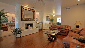 A spacious living room with a fireplace, a large mirror, and a ceiling fan.