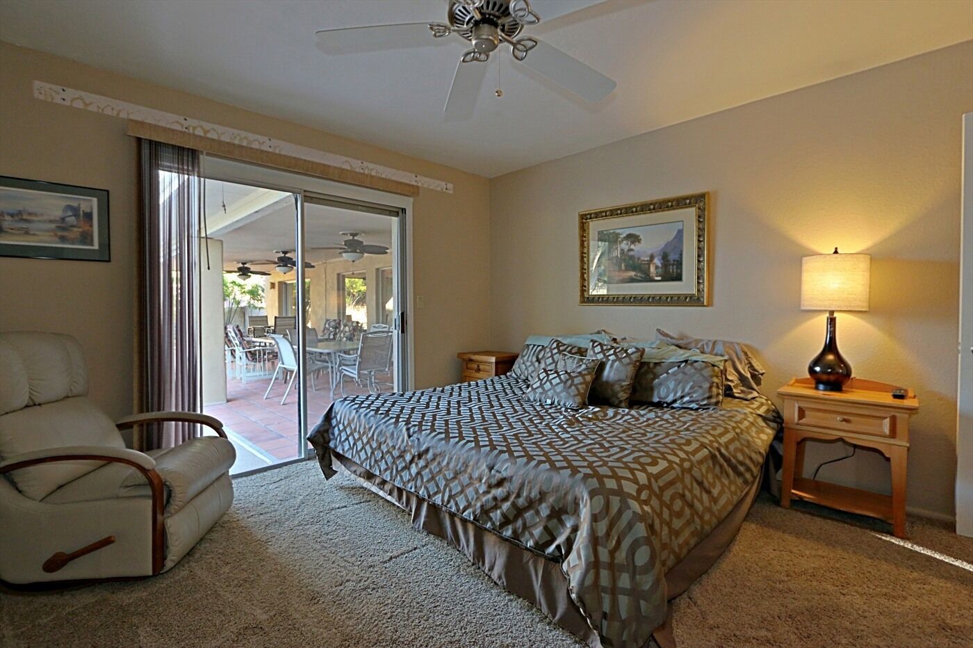 A bedroom with a bed, a chair, a nightstand, a lamp, and a ceiling fan.