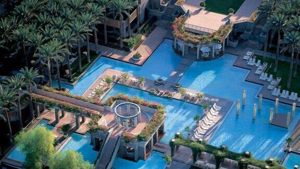 An aerial view of a resort with multiple swimming pools, palm trees, and lounge areas.