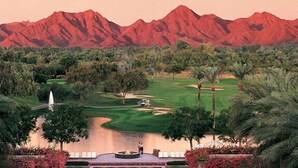 A golf course with a water feature, palm trees, and a mountain range in the background.