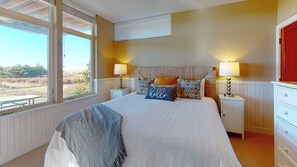 Une chambre à coucher avec un grand lit, deux tables de chevet, une fenêtre donnant sur un beau paysage et une porte rouge.