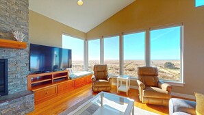 A spacious living room with a large flat-screen TV, leather armchairs, and a view of a vast landscape through large windows. - OCEAN FRONT: MODERN MARVEL: Seaside Vacation Homes, Inc Managed Property (Gearhart)