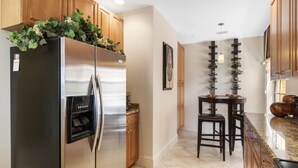 Una cocina con armarios de madera, un refrigerador de acero inoxidable, un horno empotrado y un pequeño comedor con dos sillas.