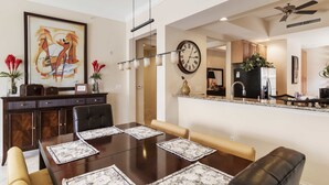 Un comedor con una mesa de madera, sillas acolchadas y un reloj en la pared.