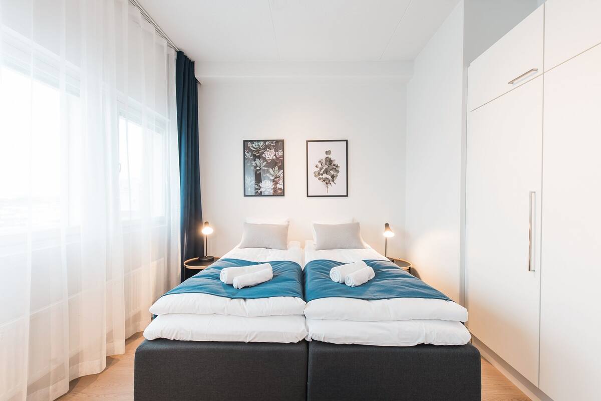 Een moderne hotelkamer met een tweepersoonsbed, twee nachtkastjes en een kledingkast.