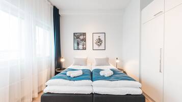 A modern hotel room with a double bed, two bedside tables, and a wardrobe.