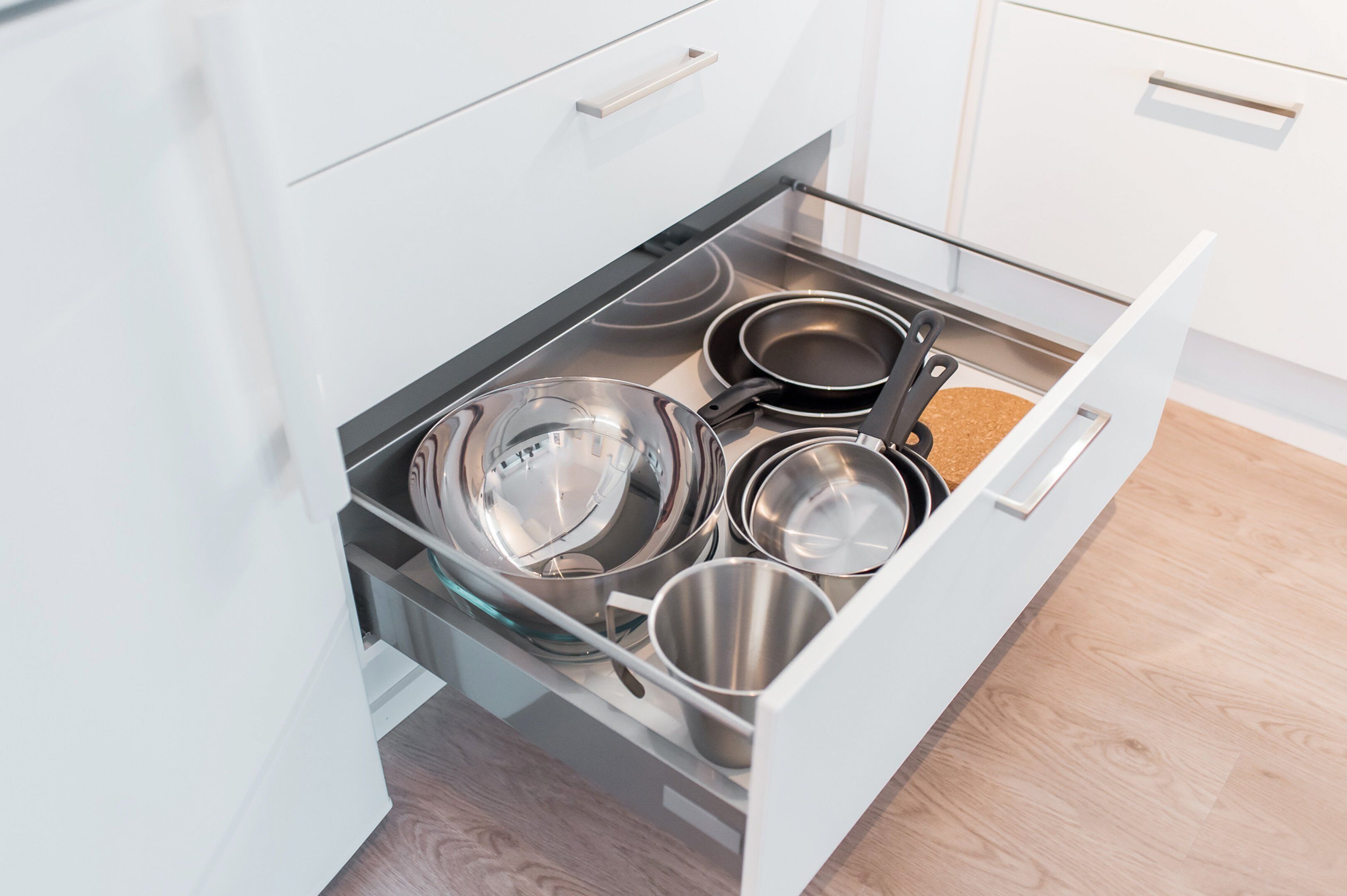 Un caj ón de cocina con utensilios de acero inoxidable, incluyendo ollas, sartenes y una tetera.