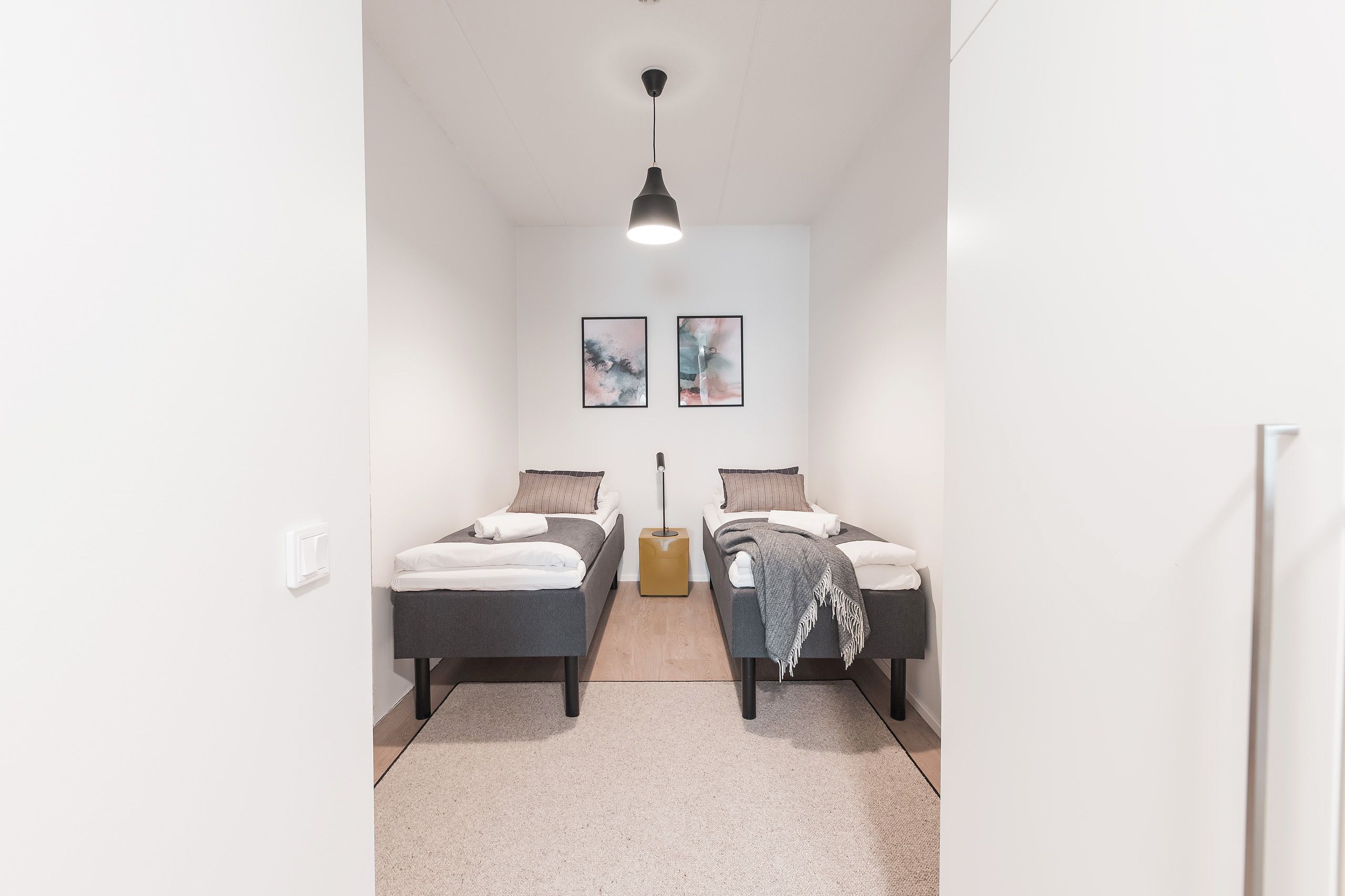A modern bedroom with two single beds, a bedside table, a lamp, and two framed pictures on the wall.
